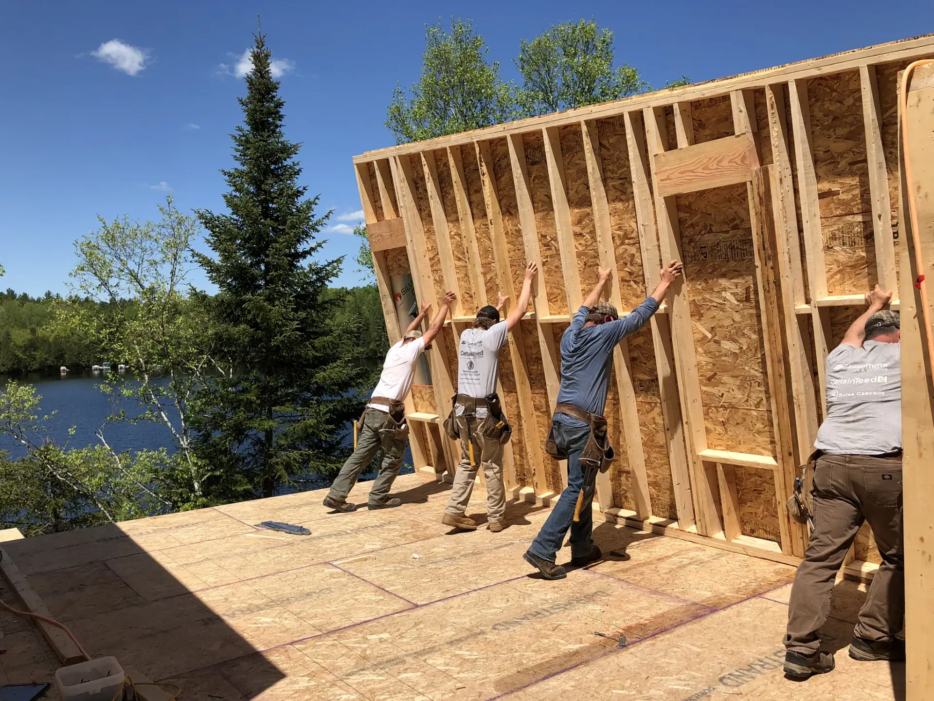 Four workers raising a wooden wall frame on a lakefront building site